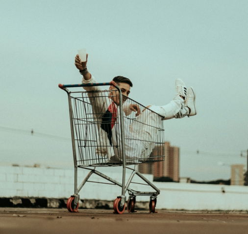 woman in white jacket and blue denim jeans riding on shopping cart during daytime