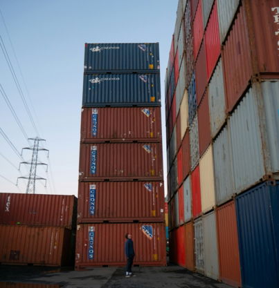 man in blue shirt walking near red cargo containers during daytime